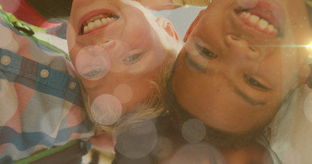 Image of light spots over happy diverse schoolboys in huddle on sports field. Frienship, health,...