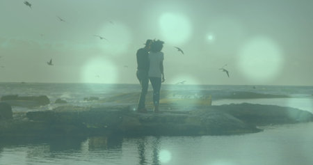 Image of light spots over biracial couple at beach. Holidays, free time and love concept digitally generated image.の写真素材