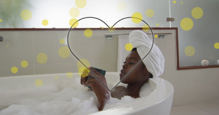 Image of heart over african american woman drinking coffee. Relaxing, coffee and digital interface concept digitally generated image.の写真素材