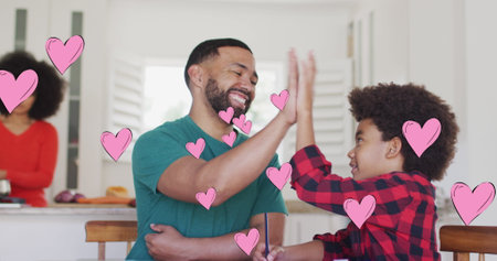 Image of social media heart icons over smiling biracial man and son high fiving. global communication, connections and social media concept digitally generated image.の写真素材