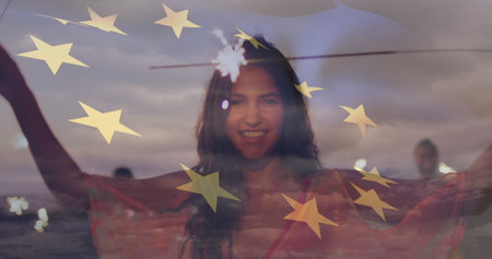 Image of flag of european union over happy biracial woman with sparklers on beach. american patriotism and independence concept digitally generated image.の写真素材