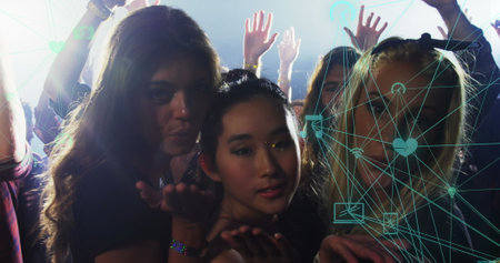 Image of connections with icons over biracial women sending kisses at concert. music, entertainment, fun and connections concept digitally generated image.の写真素材