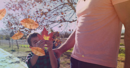 Image of leaves over happy caucasian father and daughter in park. family, and spending time together concept digitally generated image.の写真素材