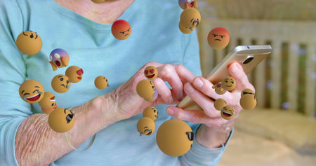 Image of emoticons floating over hands of caucasian senior woman using smartphone. global network, connections, social media and technology concept digitally generated image.の写真素材