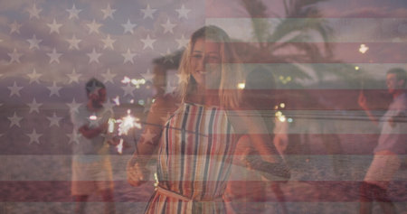 Image of flag of united states of america over happy diverse friends with sparklers on beach....