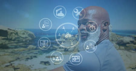 Image of media icons over smiling senior african american man at beach. healthy, active lifestyle, connections and digital interface concept digitally generated image.の写真素材