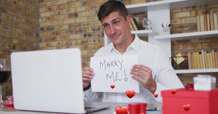 Image of red hearts flying over caucasian man proposing on laptop image call. valentine&#39;s day, love and romance concept digitally generated image.の写真素材