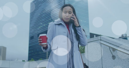 Image of lens flare over biracial woman walking to work, using smartphone in street. walk to work day, commuters on the go in the city digitally generated image.の写真素材