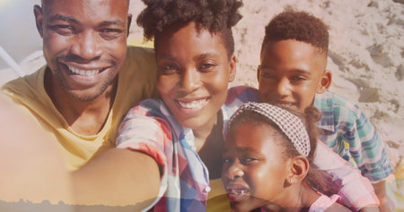 African American family enjoying time on beach, father holding camera. All have dark hair, father wearing yellow shirt, mother in blueの写真素材