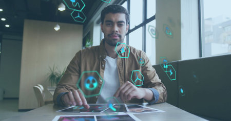 Image of icon in circles over biracial man sitting on chair and looking at camera in office. Digital...