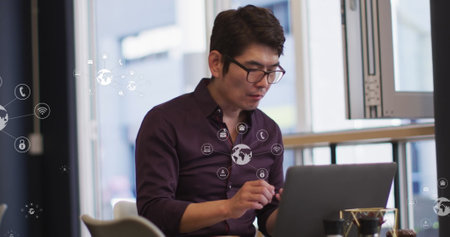 Asian male in his middle age, wearing glasses, focusing on laptop. He has short black hair, wearing...
