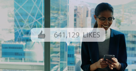 Image of like icon with growing number over biracial businesswoman using smartphone. Global business, finances and digital interface concept digitally generated image.の写真素材