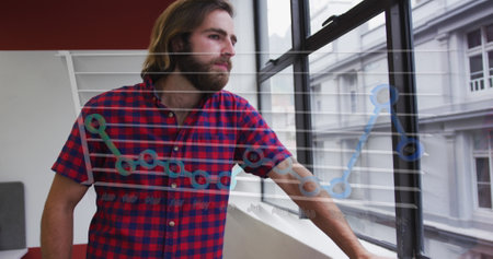 A young Caucasian professional wearing red plaid shirt, gazing out a window. Sporting long brown hair and a beard, standing in a modern office with a white backgroundの写真素材