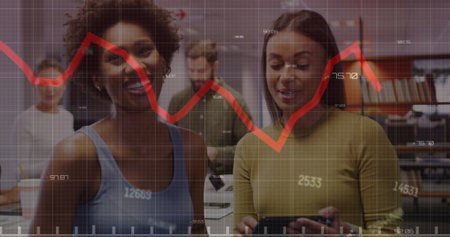 Image of changing numbers and red graph against two diverse women discussing at office. Computer interface and business data technology conceptの写真素材