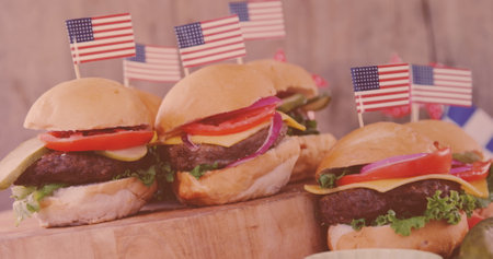 Four burgers, each topped with American flag, resting on wooden board. Featuring lettuce, tomato, cheese, and beef patties, offering a tempting displayの写真素材