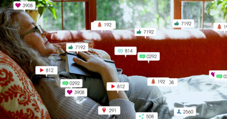 Image of social media icons over caucasian senior woman with book sleeping on the couch at home. Social media networking technology conceptの写真素材