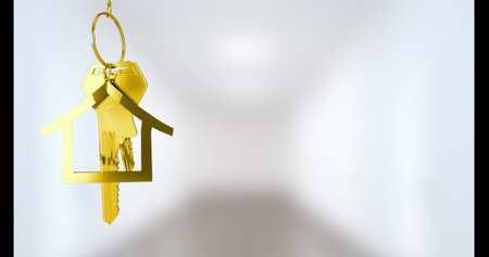 Golden house-shaped keychain hanging against soft white background. Light casting shadows, creating a subtle, dreamy effect on surfaceの写真素材