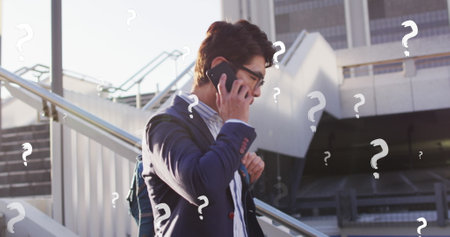 Image of question marks over asian businessman talking on cellphone while moving down steps. Digital composite, multiple exposure, confusion, sign, puzzle, business and technology concept.の写真素材