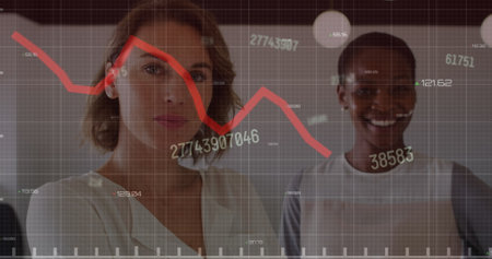 Image of changing numbers and red graph over portrait of two diverse women smiling at office. Computer interface and business data technology conceptの写真素材