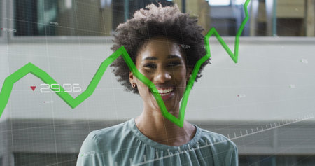 Image of graphs with changing numbers over smiling african american woman standing in office. Digital composite, multiple exposure, report, growth, digits, portrait and business concept.の写真素材