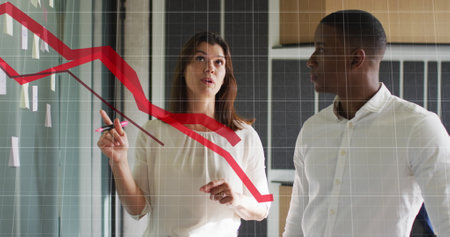 Image of red graphs moving over diverse man and woman discussing over memo notes at office. Computer...