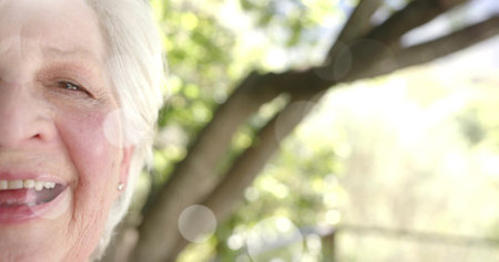 Image of spots of light and trees over smiling senior caucasian woman in garden. Happiness, senior...