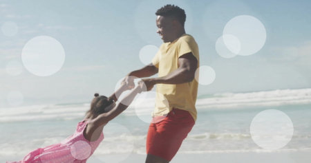 Image of light spots over african american father and daughter playing on beach. Fatherhood, childhood, lifestyle, togetherness and family concept digitally generated image.の写真素材