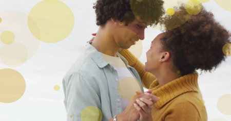 Image of light spots over happy biracial couple dancing on beach. Relationship, lifestyle, togetherness and love concept digitally generated image.の写真素材