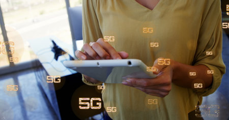 Image of multiple 5g text over midsection of biracial woman standing and using digital tablet. Digital composite, multiple exposure, business, office, telecommunication and technology concept.の写真素材