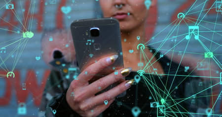 A young Caucasian professional holding smartphone, digital icons floating around. Wearing a black jacket, focusing on screen, she showcases light brown hairの写真素材