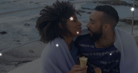 Image of glowing star icons over african american couple embracing each other at the beach. Love and...