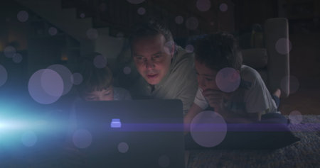 Image of light and dots moving over happy caucasian man with kids using laptop. Family, spending...