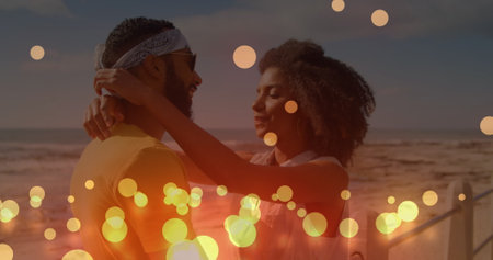 Image of glowing yellow spots over african american couple embracing each other at the beach. Love and relationship conceptの写真素材