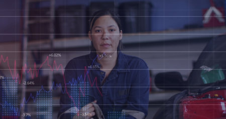 Image of female mechanic cleaning her hands with a cloth at a car service station over graphs. global shipping and connections concept digitally generated image.の写真素材