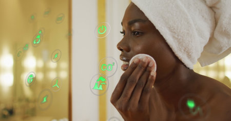 Image of icons over african american woman cleansing face in bathroom. Global lifestyle, self care and digital interface concept digitally generated image.の写真素材