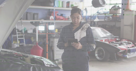 Image of financial data processing over biracial female car mechanic using tablet. Global business, finance and data processing concept digitally generated image.の写真素材