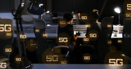Image of multiple 5g texts over rear view of diverse coworkers discussing reports in office. Digital...