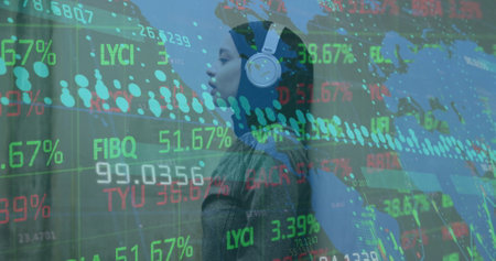 Image of graphs, map, trading board, biracial woman wearing hijab listening to music. Digital...