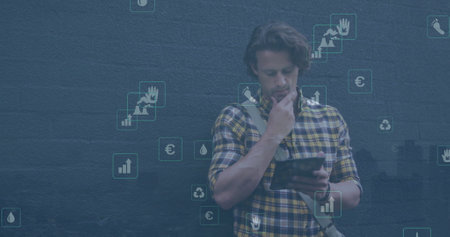 Image of multiple icons over caucasian man standing beside bicycle and using digital tablet. Digital composite, multiple exposure, hazardous, environment, transportation and technology concept.の写真素材