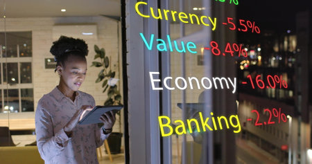 Image of financial data over african american businesswoman using tablet at office at night. Work, connection, business, digital interface and communication, digitally generated image.の写真素材