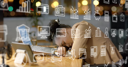 Image of business icons over tired african american businesswoman waking up at office desk. Overwork, connection, business, digital interface and communication, digitally generated image.の写真素材