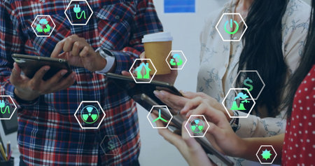 Image of ecology icons over diverse colleagues using tablet in office. Business, technology and...