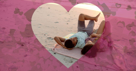 Image of hearts moving over diverse couple in love lying on beach in summer. Love, romance, valentine&#39;s day and vacation concept digitally generated image.の写真素材