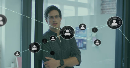 Image of network of connections with icons over caucasian businessman smiling in office. Technology, business and digital interface concept digitally generated image.の写真素材