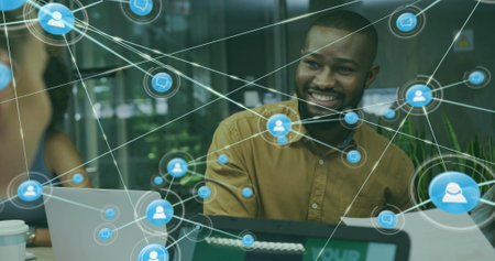 Image of network of connections with icons over diverse colleagues using laptop in office. Technology, business and digital interface concept digitally generated image.の写真素材