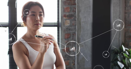 Image of digital icons, connections and data processing over asian businesswoman in office. Global finance, business, connections, computing and data processing concept digitally generated image.の写真素材