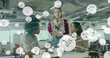 Image of network of connections with icons over diverse female colleagues using tablet in office. Technology, business and digital interface concept digitally generated image.の写真素材