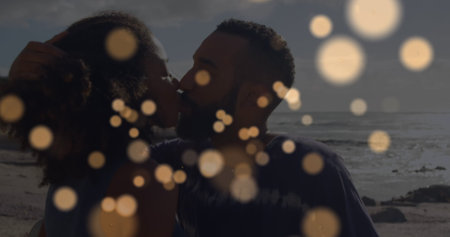 Image of yellow spots over african american couple embracing each other at the beach. Love and relationship conceptの写真素材