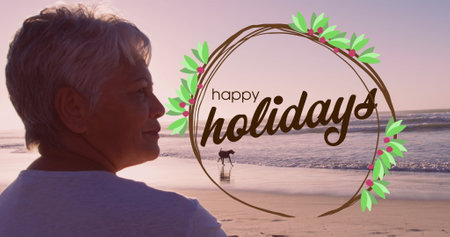 Image of happy holidays over biracial senior woman on beach. Christmas, holidays, celebration and relax concept digitally generated image.の写真素材