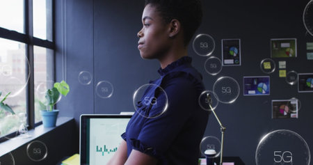 Image of multiple 5g text banner over african american woman looking out of window at office. Computer interface and business technology conceptの写真素材